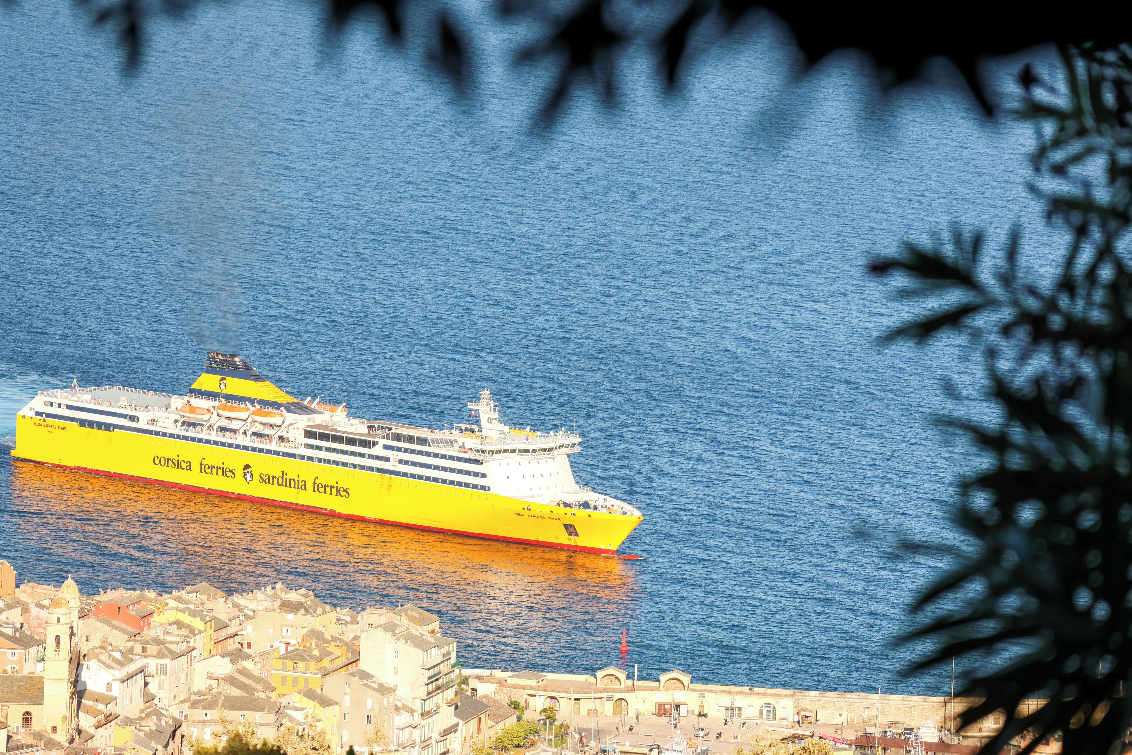 A large yellow cruise ship named 'MEGA EXPRESS THREE' docked at a port with a cityscape in the background.