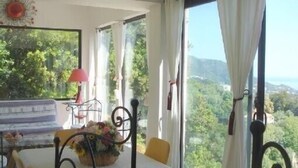 A room with a table set for dining, a window with curtains, and a view of greenery outside. - Ground floor of beautiful villa T2 - 70 m2 - 4 people with magnificent sea views (Bastia)