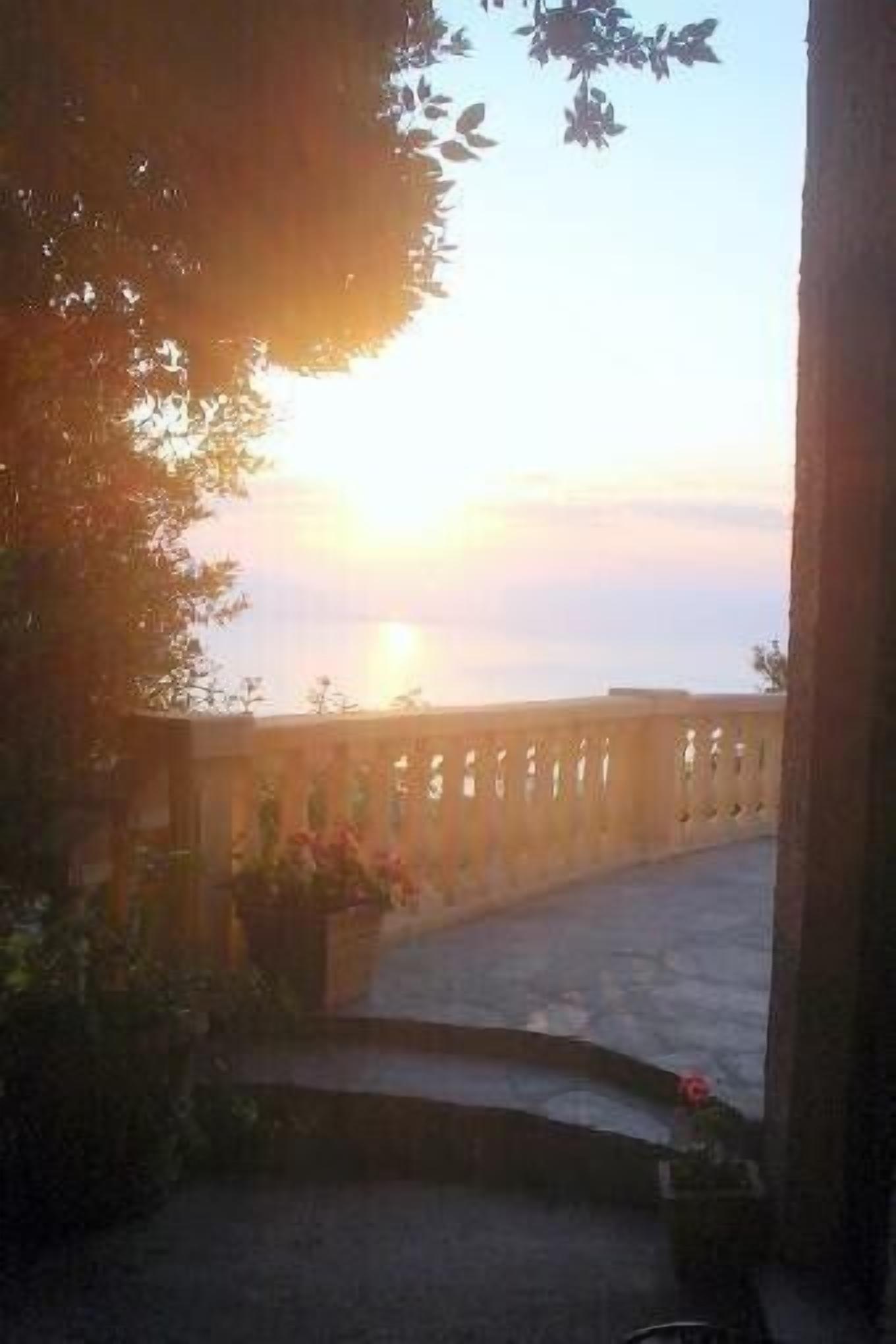Sonnenuntergangblick von einem Balkon mit Steinbrüstung und Pflanzen in Töpfen.