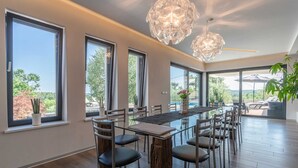 A modern dining area with a glass table, multiple chairs, and large windows offering views of the outdoors. - Beautiful modern 4-BR villa for 8 with pool in Istria (Pican)