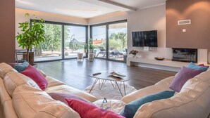A spacious living room with a large window, a flat-screen TV, and a fireplace. - Beautiful modern 4-BR villa for 8 with pool in Istria (Pican)