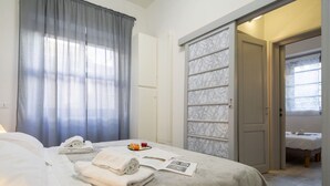 Hotellihuone, jossa on sänky, vaatekaappi, avoimesta ovesta näkyvä kylpyhuone ja ikkuna, jossa on verhot.
