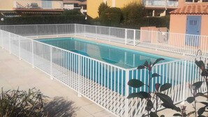 Piscina cercada por um muro branco, com edifícios com varandas e um céu azul claro.