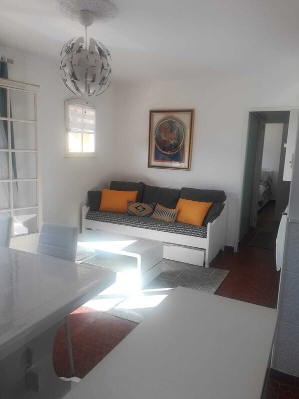 A modern living room with a white sofa, orange cushions, a dining table, and a unique spherical ceiling light.