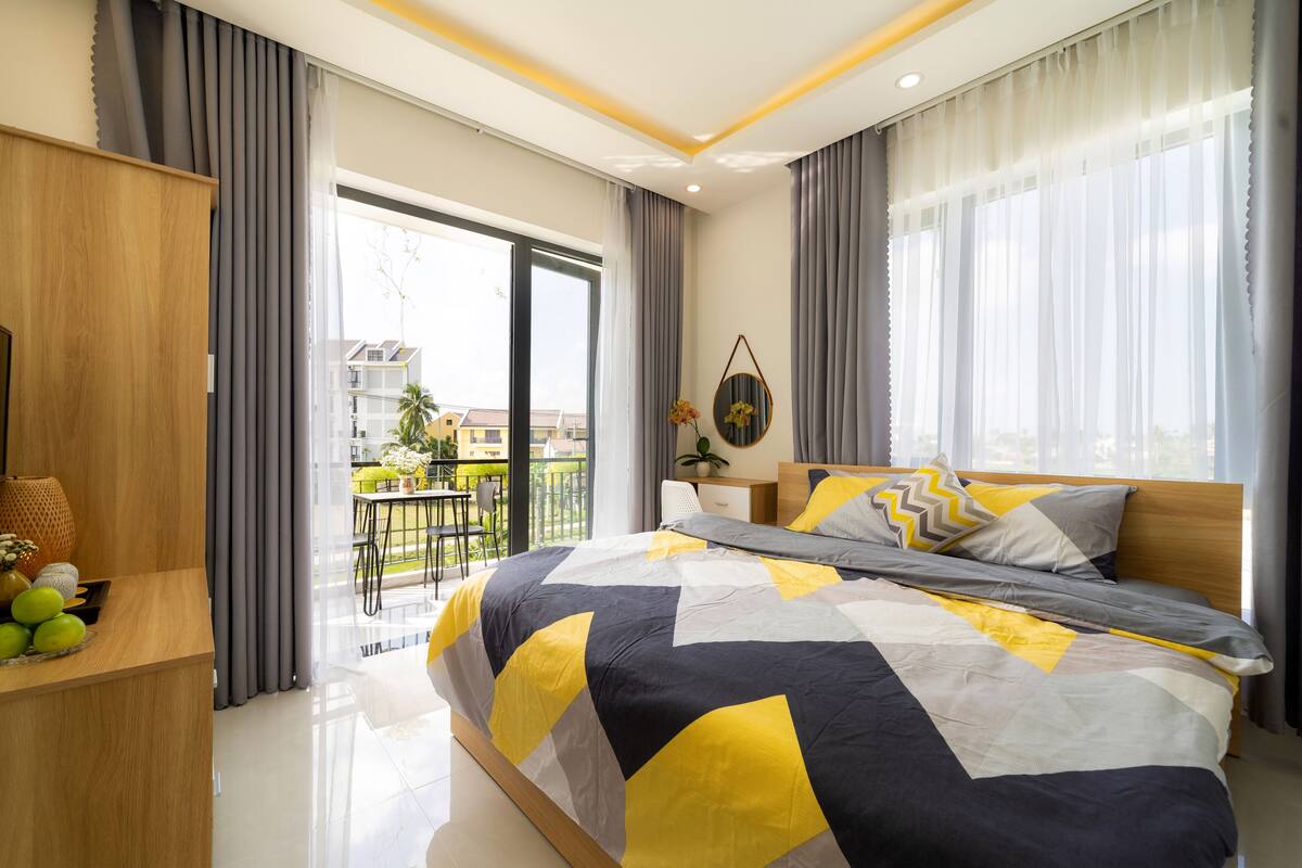 Ein modernes Schlafzimmer mit einem großen Bett, einem Holzschrank, einem Schreibtisch mit Lampe und Blick auf den Balkon.