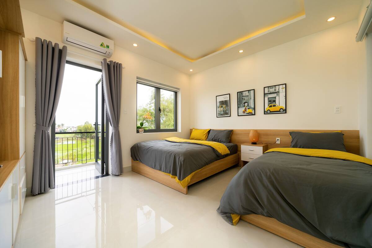 Ein modernes Schlafzimmer mit zwei Betten, einem Balkon und Blick auf Grünflächen.