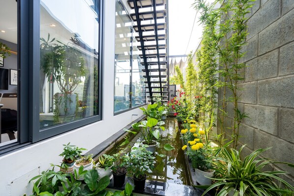Un petit jardin intérieur, avec un élément décoratif à base d’eau, des plantes en pot et une structure en bambou.