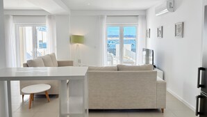 Una sala de estar moderna con un sofá, una mesa de comedor y vistas al mar a través de amplios ventanales.
