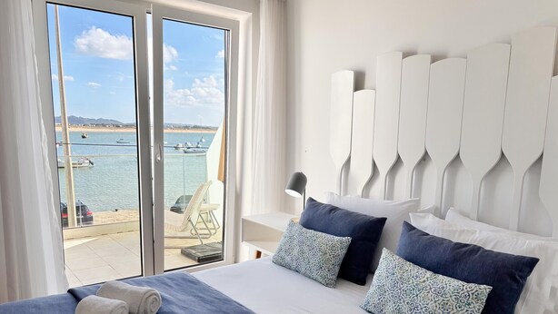 Habitación de hotel con una cama grande, vistas al mar y un balcón con una silla.