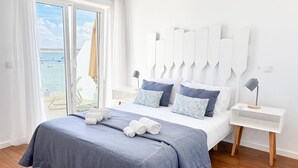 Un dormitorio moderno con una cama grande, dos mesitas de noche y vistas al mar a través de un ventanal corredera.