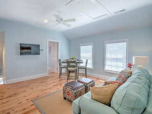 A spacious living room with a ceiling fan, a dining area with a table and chairs, and a light blue sofa with patterned ottomans. - Downtown St. Michaels | Walk to Shops, Restaurants and Nightlife (St. Michaels)
