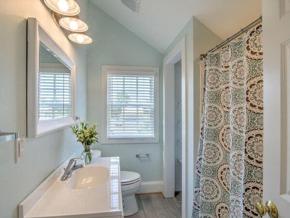 A bathroom with a white sink, a mirror, and a shower curtain with a floral pattern. - Downtown St. Michaels | Walk to Shops, Restaurants and Nightlife (St. Michaels)