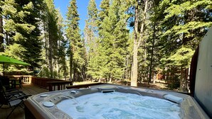 A hot tub surrounded by a wooden deck with a view of tall trees.