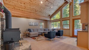 A spacious living room with a stone fireplace, a sofa set, and a large window offering a view of trees.