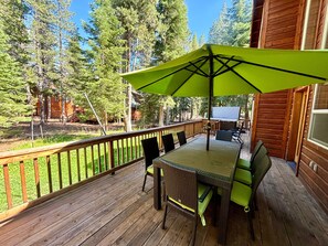 Eine Holzterrasse mit Tisch und Stühlen, einem Sonnenschirm und Blick auf einen bewaldeten Bereich.