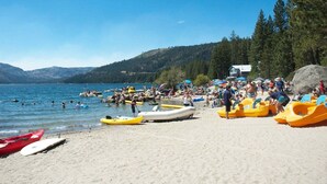 A beach with kayaks and rafts, a clear sky, and a lake in the background.