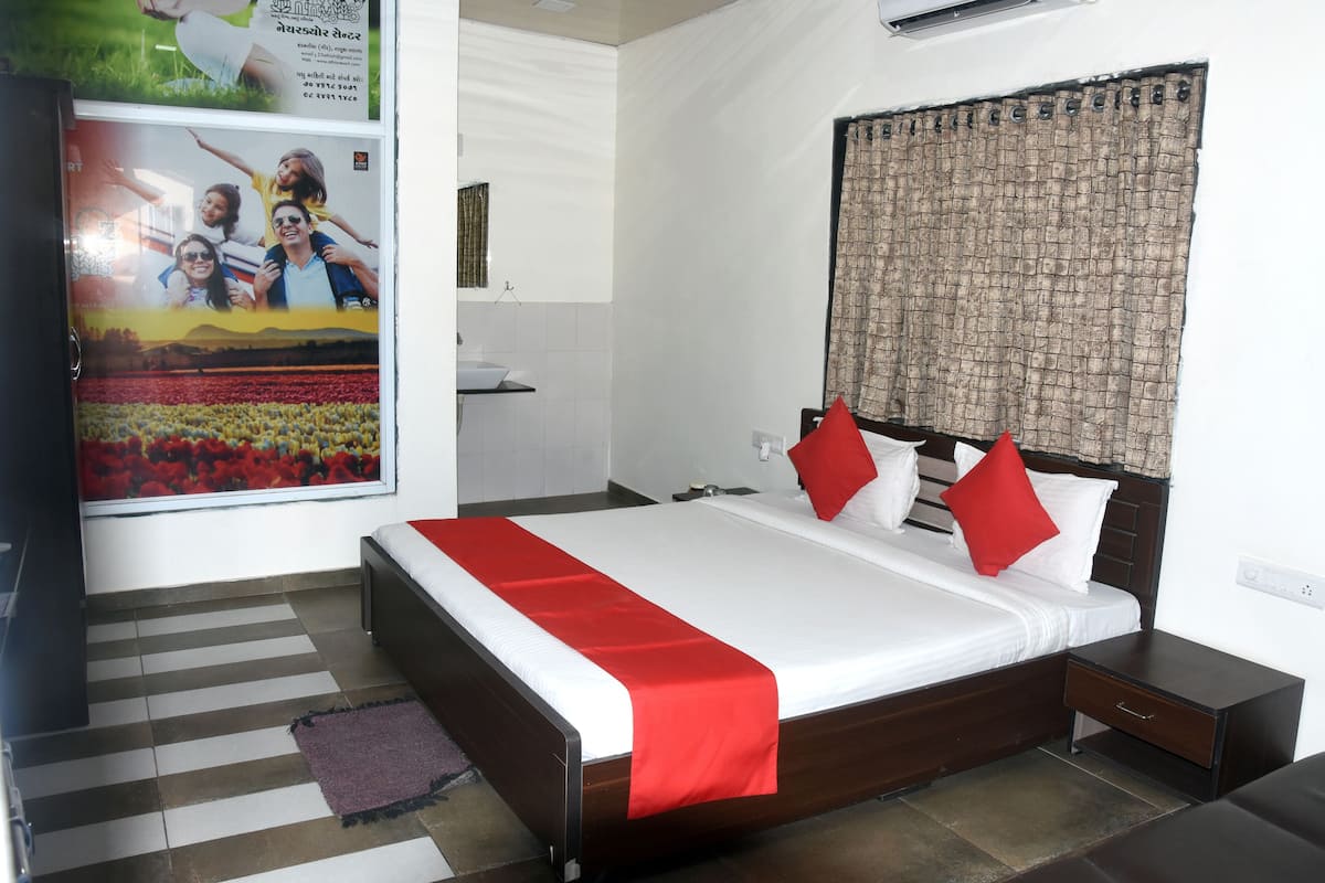 A neatly arranged hotel room with a large bed, a bedside table, a nightstand, a window with a patterned curtain, and a poster on the wall.