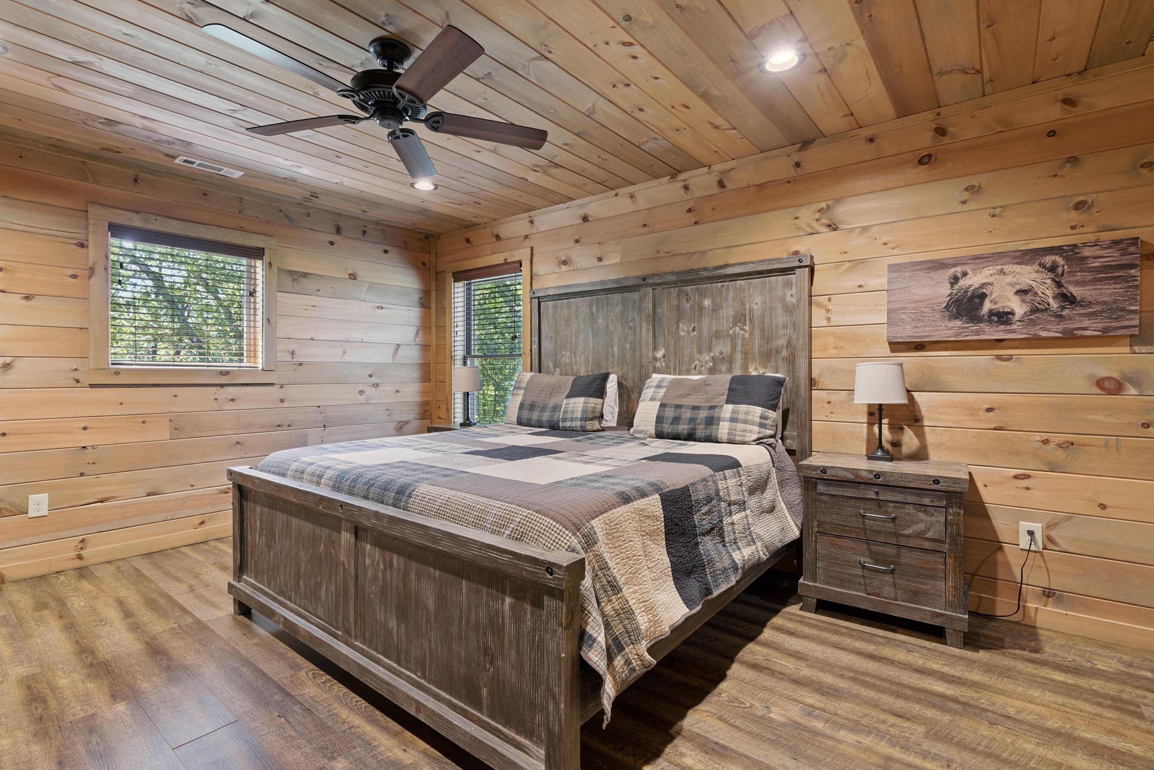 A wooden-paneled bedroom with a bed, a nightstand, a lamp, and a ceiling fan.