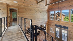 A wooden interior with a staircase, a kitchen area, and large windows offering a view of the outside.