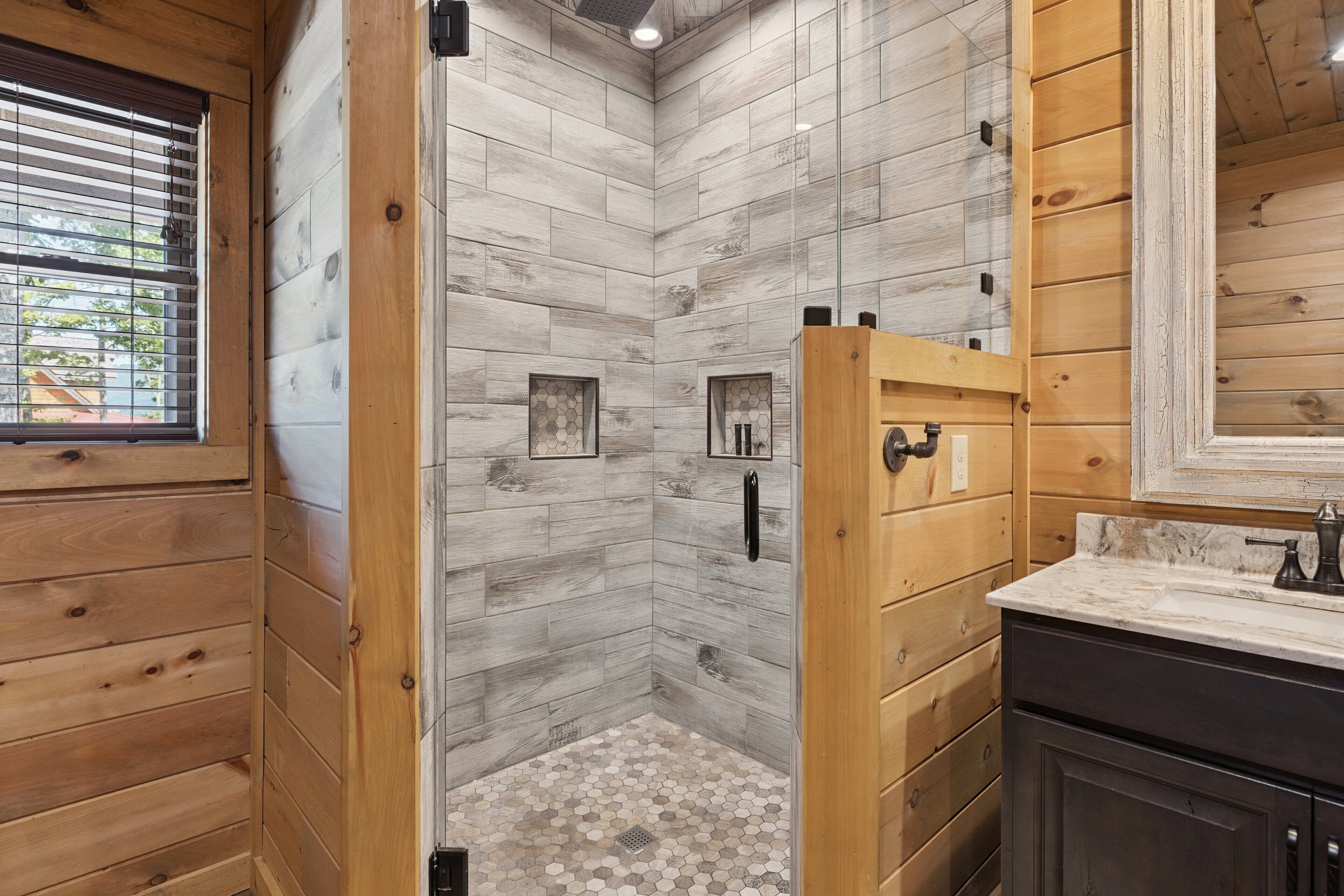 A bathroom with wooden walls, a shower with a hexagonal tile floor, and a wooden door.