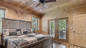 A wooden bedroom with a large bed, a ceiling fan, and a sliding glass door leading outside.
