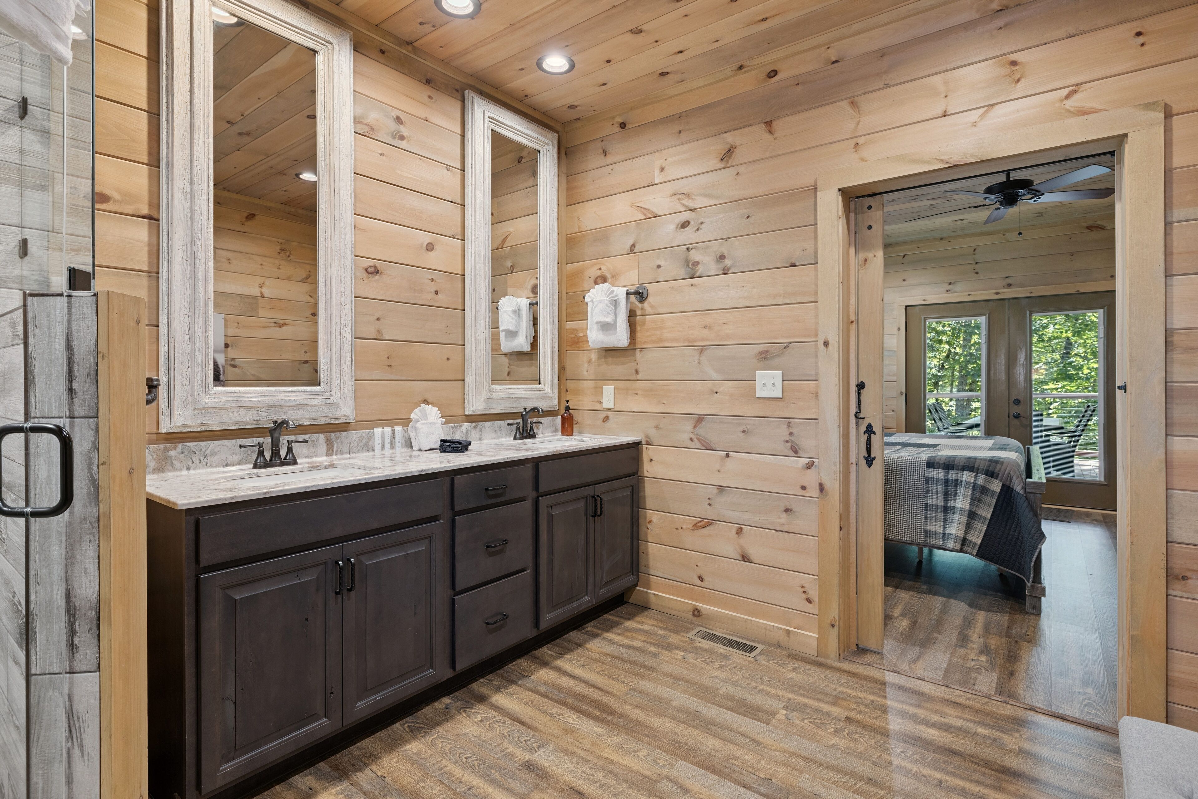 Une salle de bain de style rustique, avec des murs en bois, un grand miroir, des meubles sombres et un plancher en bois.