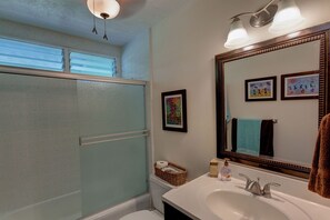 Une salle de bain avec une baignoire, un lavabo avec un miroir et un espace douche. Des tableaux encadrés ornent le mur et une serviette est accrochée au-dessus du lavabo.