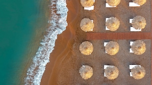 An aerial view of a beach with 12 sun umbrellas arranged in two rows of six, positioned on the sand near the shoreline. - Rubi Platinum Sign - All inclusive (Alanya)