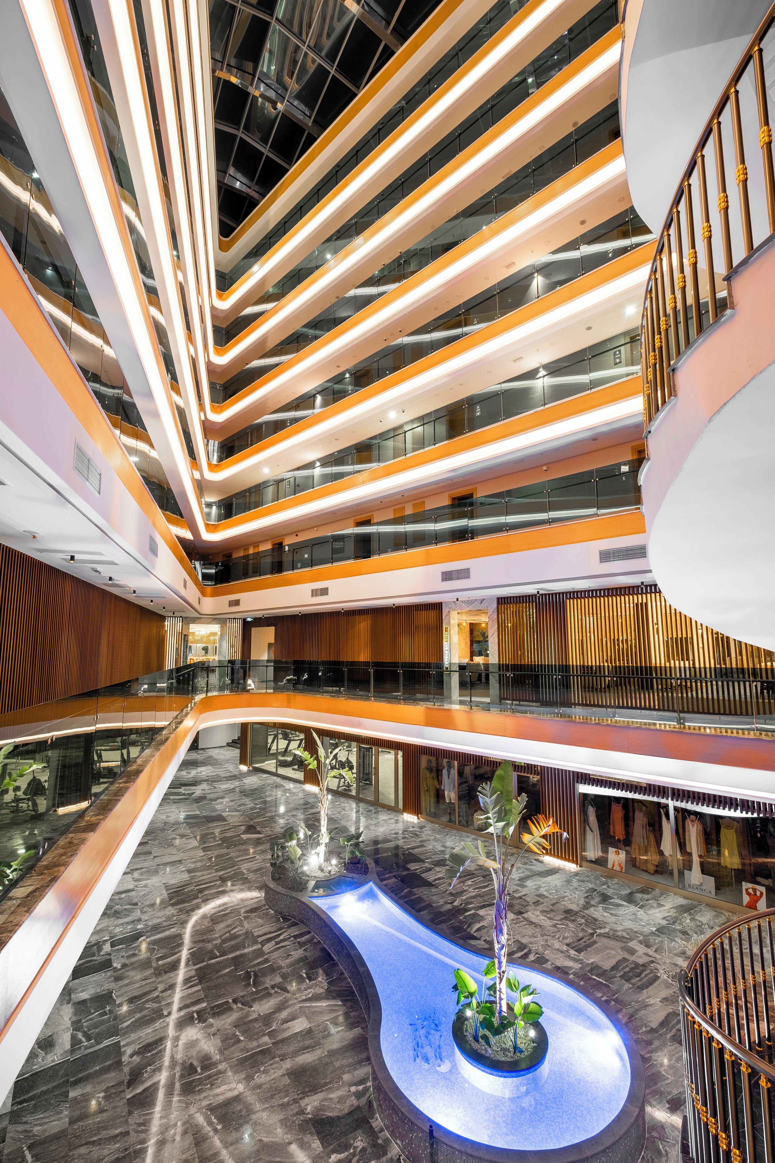 Ein mehrgeschossiges Atrium mit einem zentralen Wasserspiel, Glasgeländern und moderner Beleuchtung.