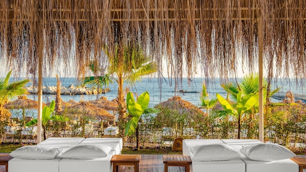 A beachside lounge with white cushioned seating and a view of the ocean. - Rubi Platinum Sign - All inclusive (Alanya)