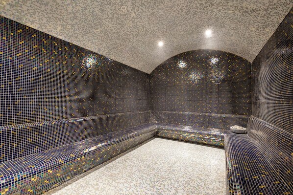 A room with a mosaic tiled wall and a seating area with a small table. - Rubi Platinum Sign - All inclusive (Alanya)