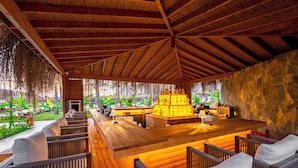 A wooden bar area with seating, a stone wall, and a view of greenery. - Rubi Platinum Sign - All inclusive (Alanya)