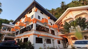 Un hôtel à plusieurs étages doté de balcons, d’un abri pour voitures et d’un jardin tropical.