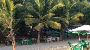 Un restaurante frente al mar con terraza al aire libre, palmeras y suelo de arena.