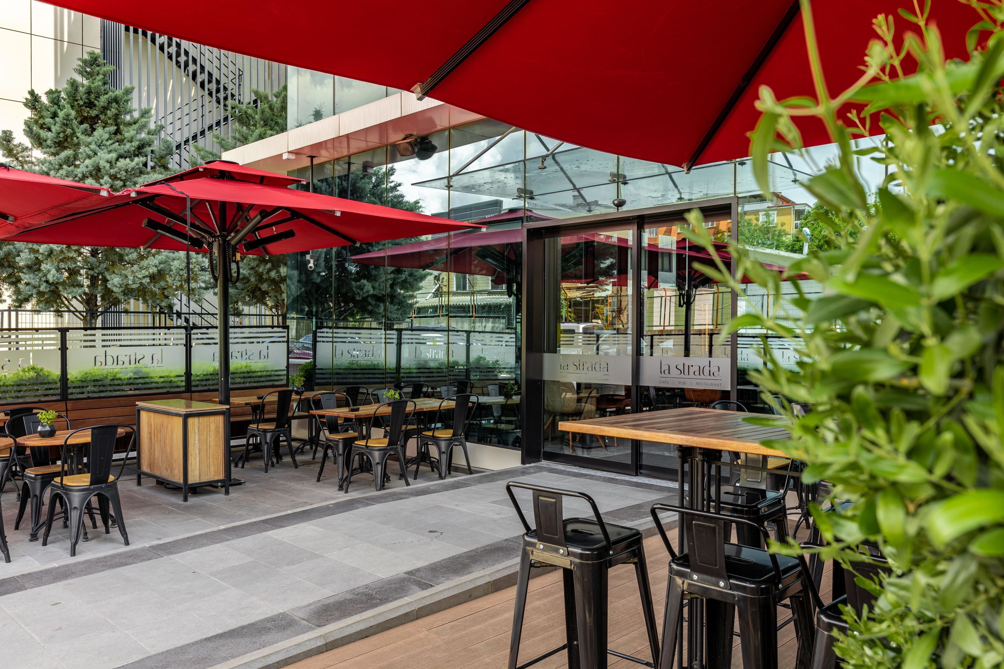 An outdoor cafe with red umbrellas, wooden tables, and black chairs.