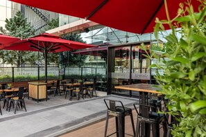 An outdoor cafe with red umbrellas, wooden tables, and black chairs.