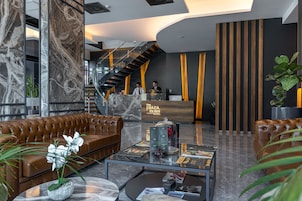 A modern lobby with a marble reception desk, leather seating, a glass coffee table, and a staircase.