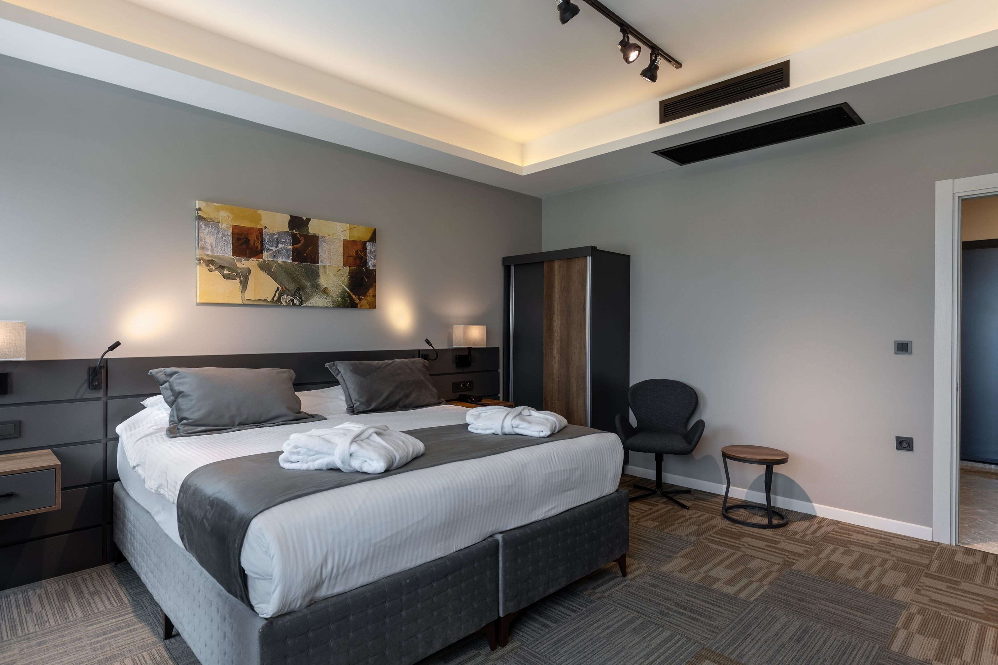 A modern hotel room with a large bed, a desk, a chair, and a painting on the wall.