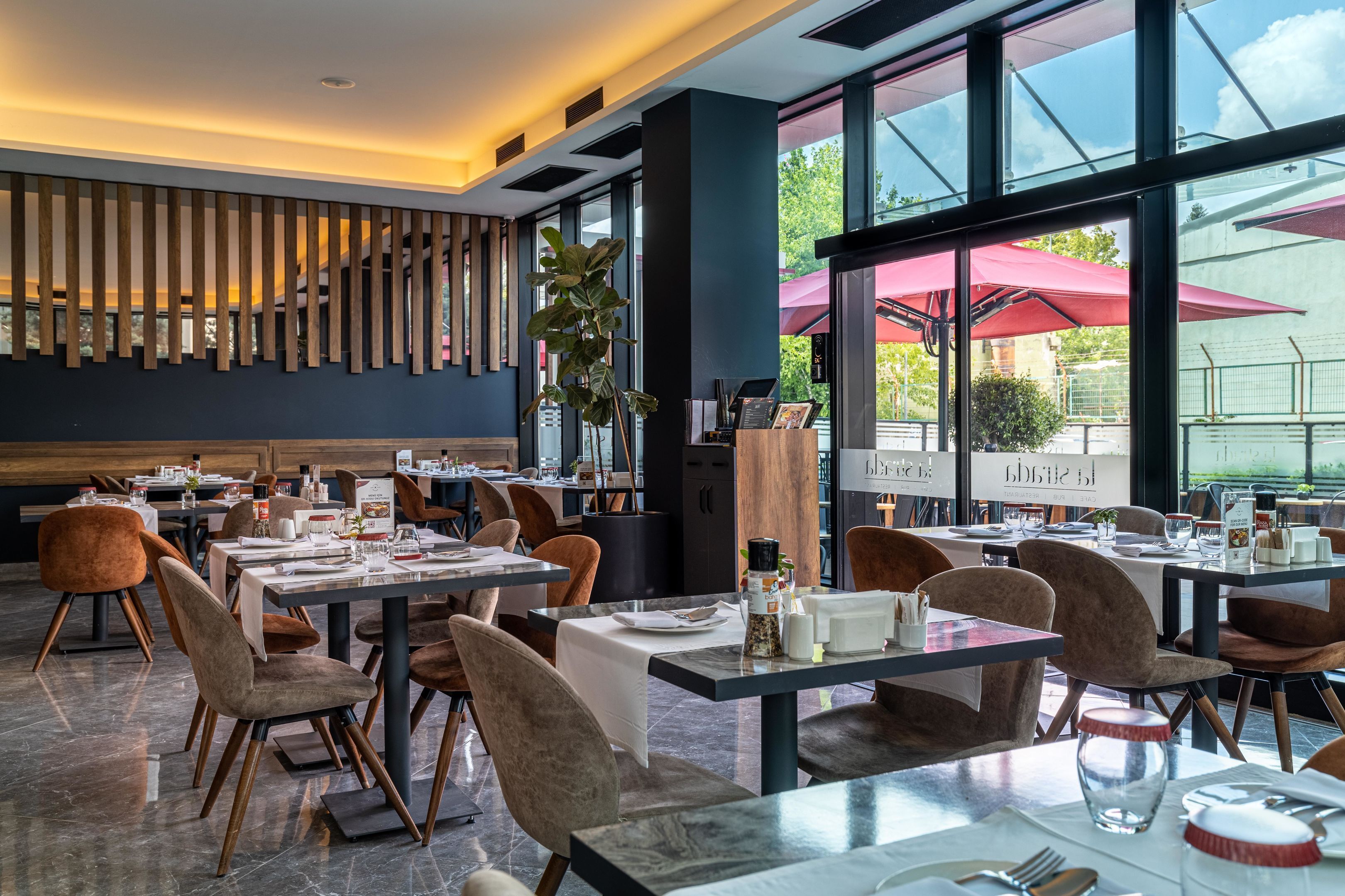 A modern dining area with tables and chairs, a large window with a view, and a wooden panel wall.