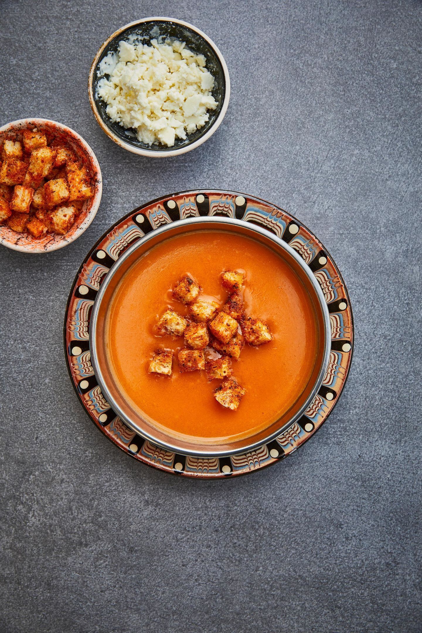 A bowl of creamy soup with croutons on a decorative plate, accompanied by a bowl of rice and a small bowl of croutons.