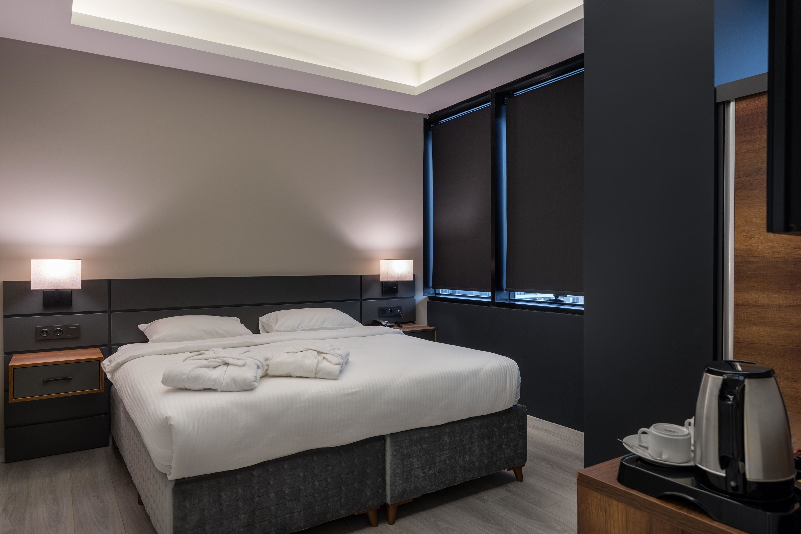 A modern hotel room with a large bed, bedside lamps, a coffee maker, and a view of the city through the window.