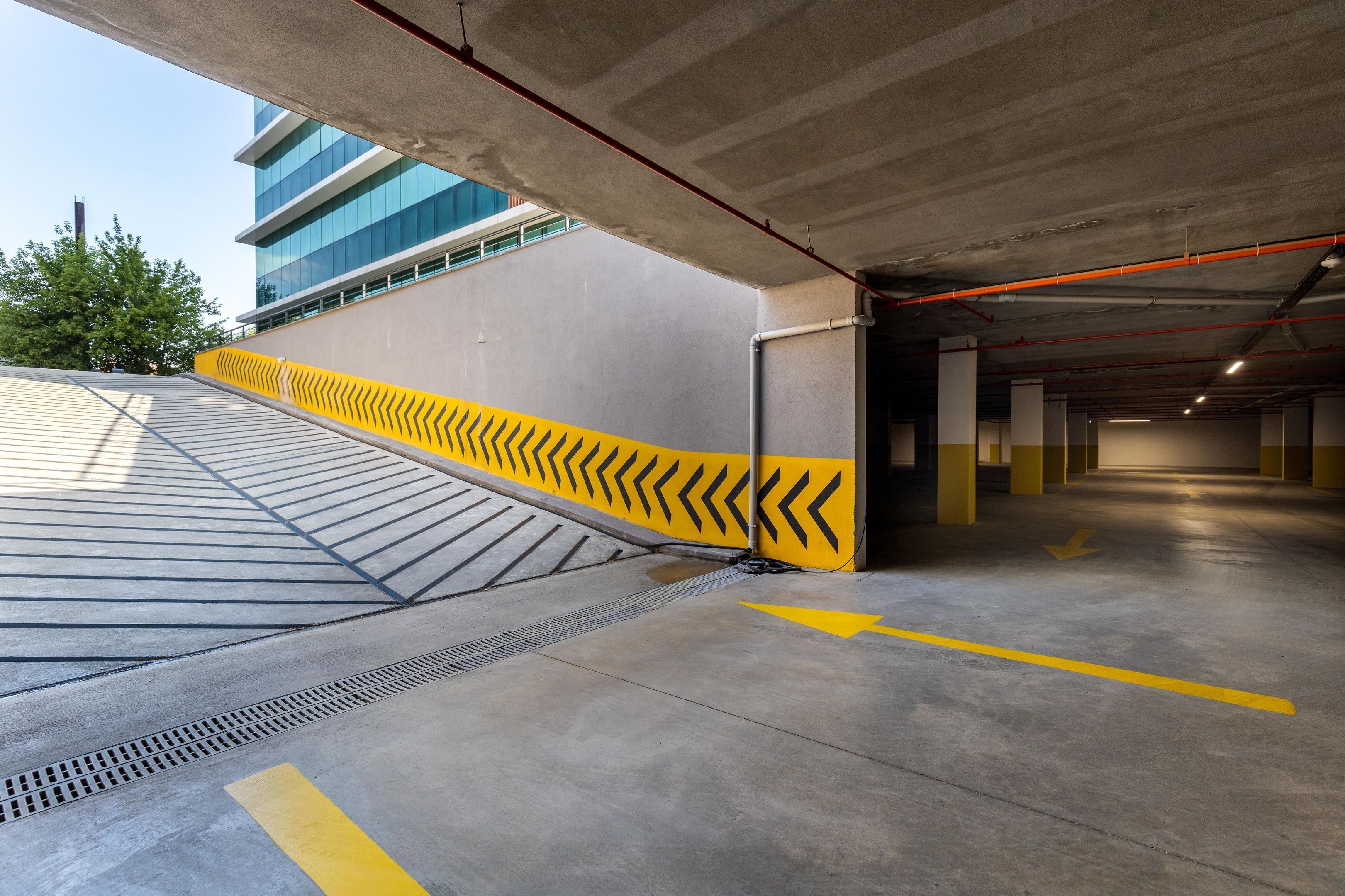 A parking garage with yellow chevron markings, concrete pillars, and a view of a modern building in the background.