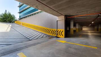 A parking garage with yellow chevron markings, concrete pillars, and a view of a modern building in the background.