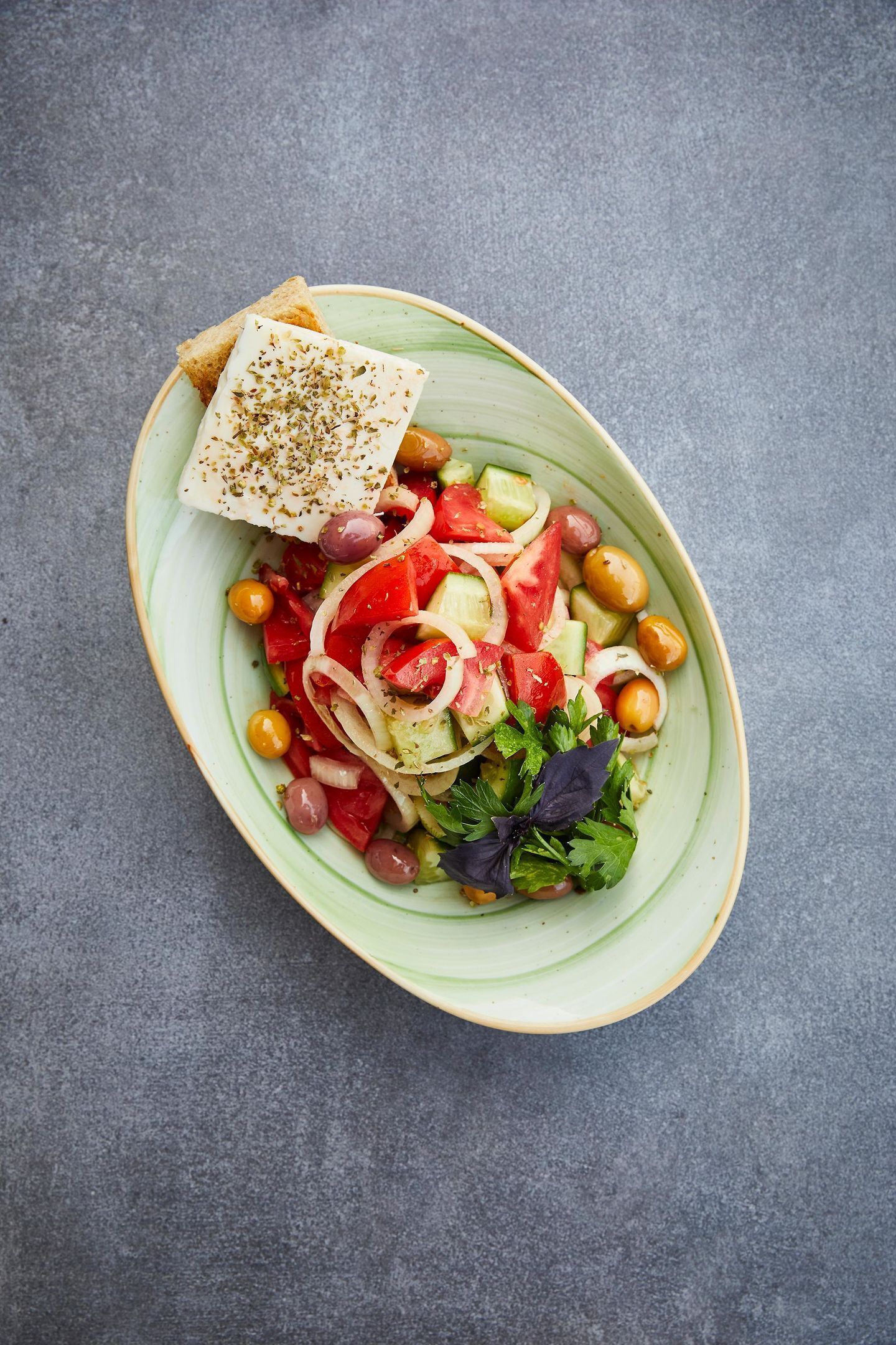 A bowl of salad with various vegetables and a piece of cheese on a plate.