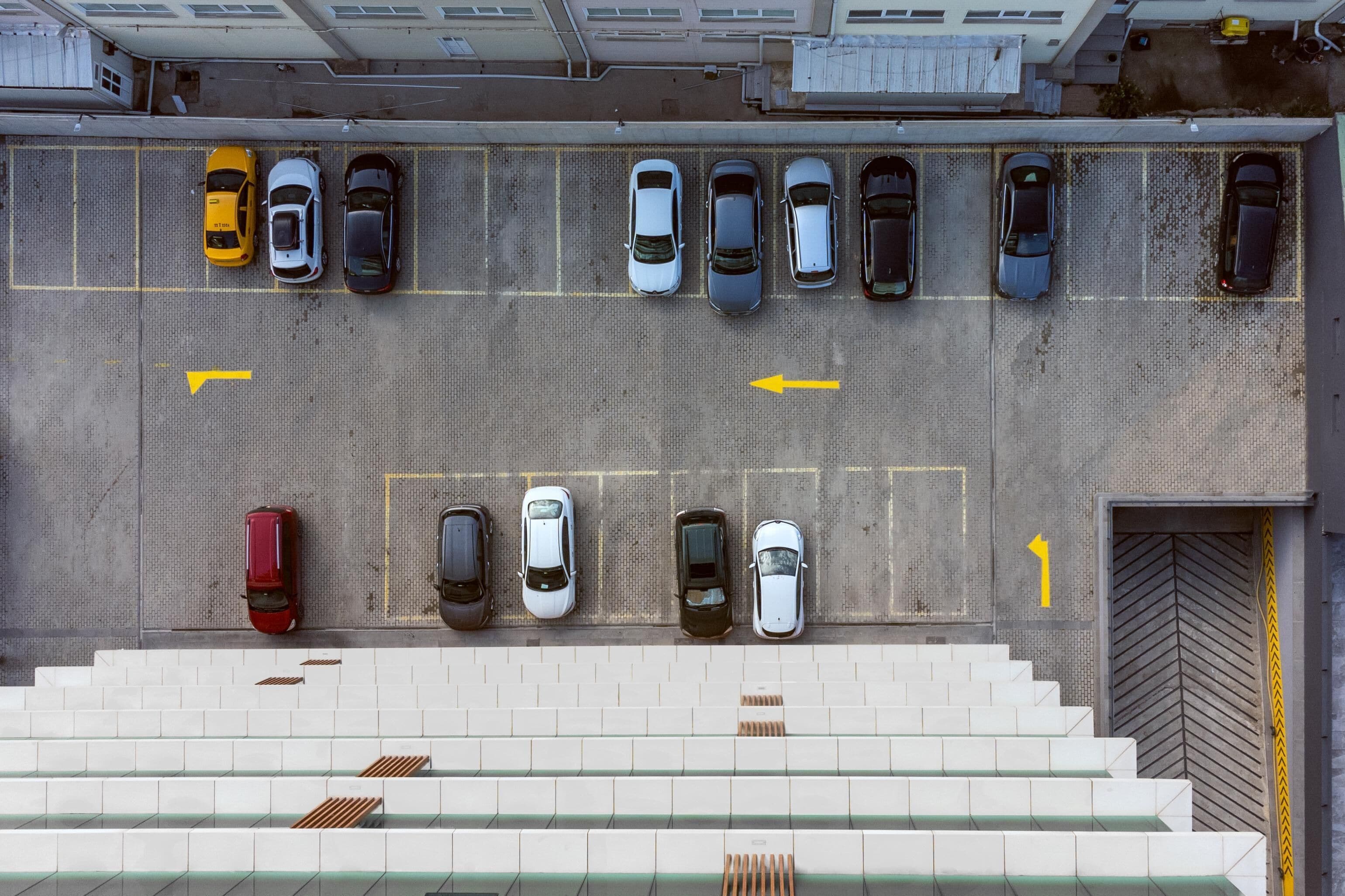 A parking lot with cars parked in rows, marked parking spaces, and a staircase leading to a building entrance.