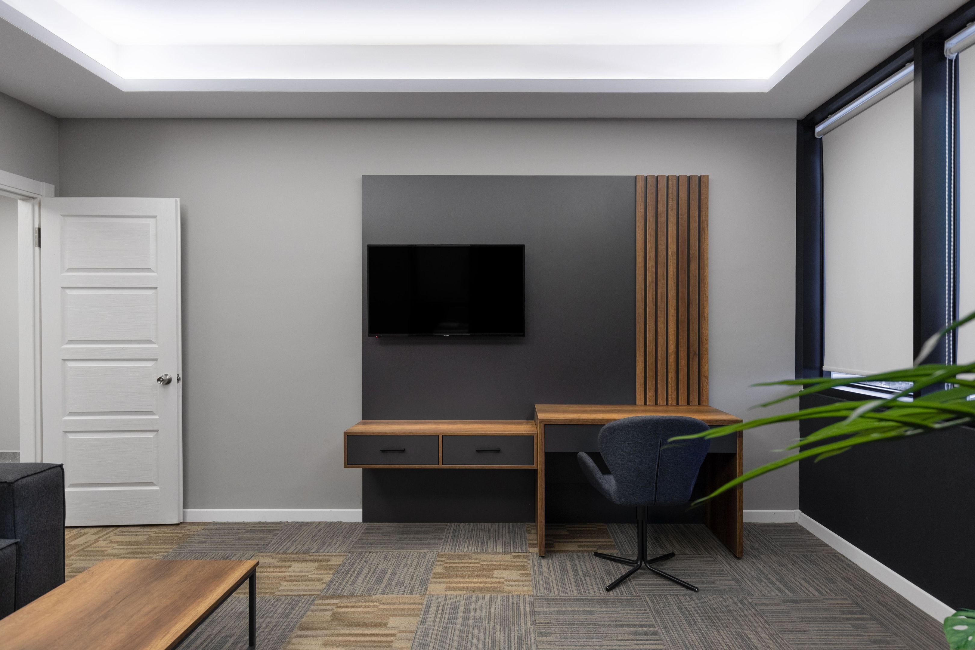 A modern room with a desk, chair, and a flat-screen TV mounted on the wall.