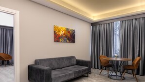 Ein modernes Wohnzimmer mit einem grauen Sofa, zwei Holzstühlen, einem runden Tisch und einem farbenfrohen abstrakten Gemälde an der Wand.