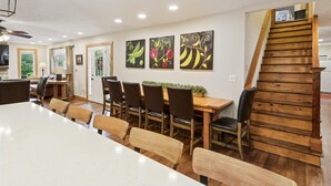 A dining area with a long table, chairs, and artwork on the wall. - Emory House 8 Bedroom Cabin by RedAwning (Pigeon Forge)
