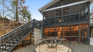 A modern building with a staircase leading to a wooden deck and a covered outdoor seating area. - Emory House 8 Bedroom Cabin by RedAwning (Pigeon Forge)