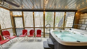 A covered outdoor area with a hot tub, red chairs, and a view of a playground. - Emory House 8 Bedroom Cabin by RedAwning (Pigeon Forge)